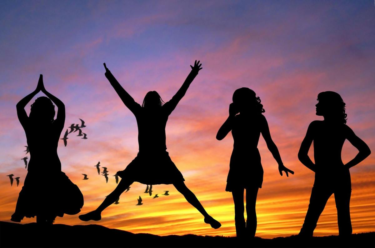 A photo of four joyful women silhouetted against a beautiful sunset.
