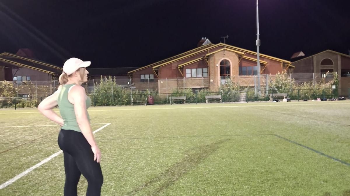 Amelia's Angels founder Ami Foxx standing to the left side of a night time brightly lit football field watching.